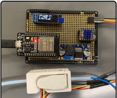 The assembled protoboard with ESP32, OLED showing a live 1.746 mm diameter reading, and the 3D-printed diameter sensor housing inline with the filament