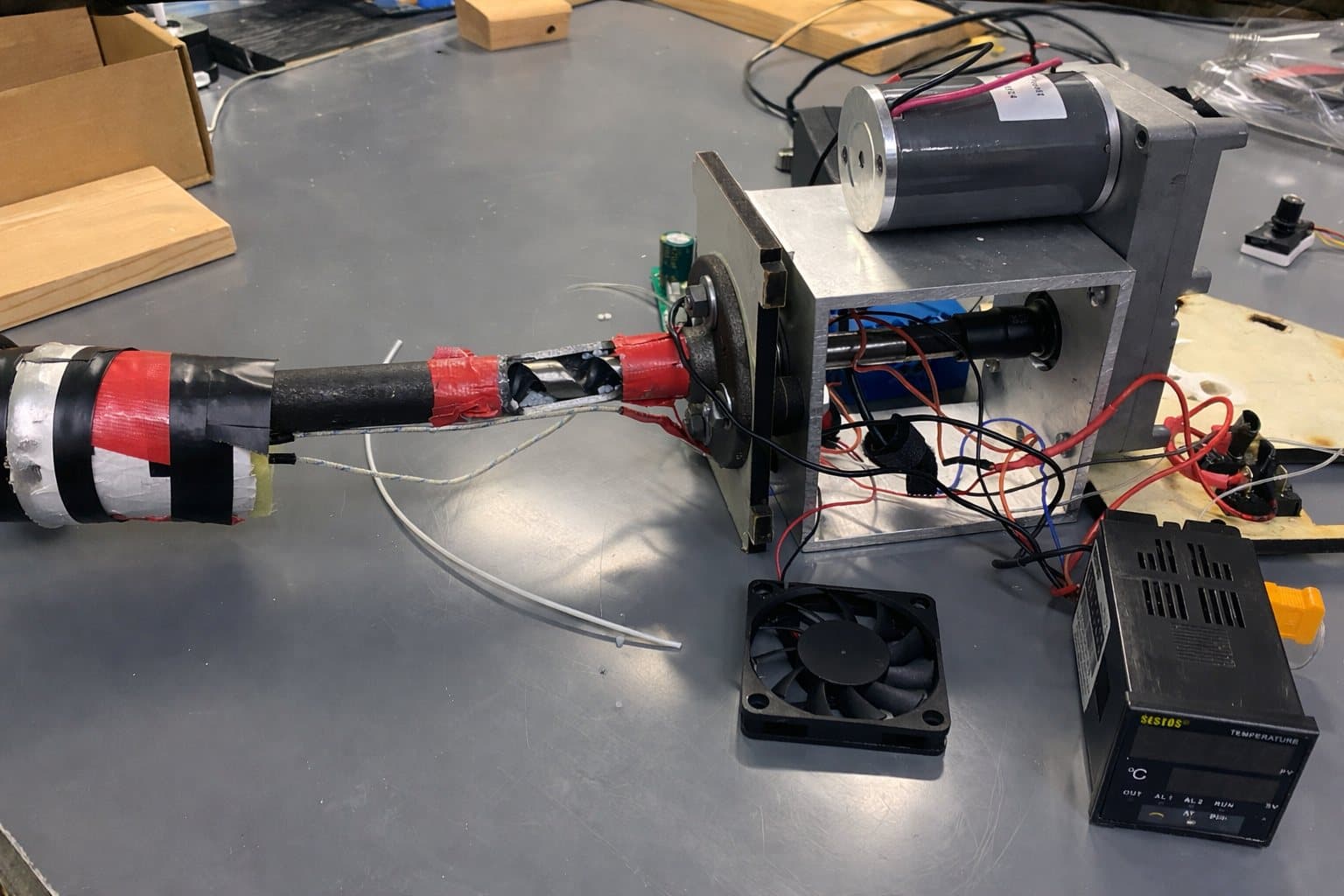 The inherited FilaStruder on the bench — horizontal barrel wrapped in tape, exposed wiring, ad-hoc temperature controller